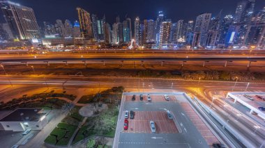 Dubai Marina gökdelenleri ve Şeyh Zayed yolu ile metro demiryolu hava geceleri. Panoramik, Birleşik Arap Emirlikleri 'nin modern kulelerinin yakınındaki bir otoyolda trafiğe bakıyor
