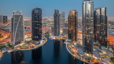 Dubai çoklu emtia merkezi karma kullanım bölgesinin bir parçası olan JLT bölge hava sahasındaki uzun binalardan geceye geçiş panoramik. Arka planda villalar