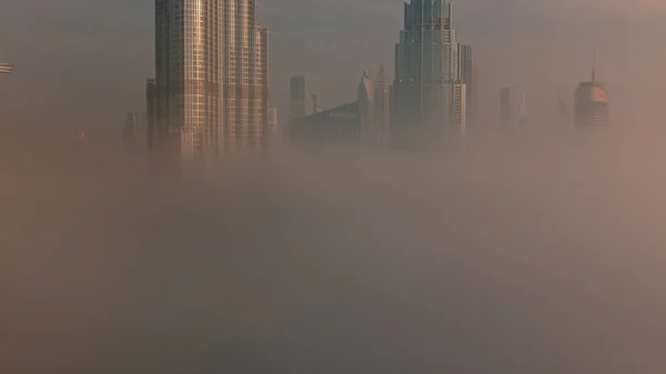 霧の中でドバイ市内の早朝の空中ビュー 高層ビルや塔がある未来的な都市のスカイラインで日の出 ガラス面から反射した太陽 — ストック写真