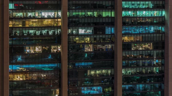 Big glowing windows in modern office buildings  at night, in rows of windows light shines. People working inside and workers make a renovation