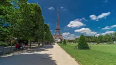 Paris 'teki Champs de Mars' taki Eyfel Kulesi. Zaman atlaması, Fransa. Yazın mavi bulutlu gökyüzü Ağaçlı yeşil çimenler ve etrafta yürüyen insanlar.