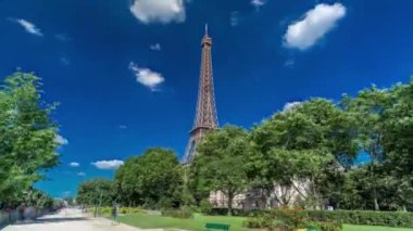 Eiffel Kulesi, Paris 'teki Siene nehri kıyılarından gösterildi. Zaman ayarlı hiperhız, Fransa. Yazın mavi bulutlu gökyüzü Yeşil ağaçlar ve etrafta yürüyen insanlar