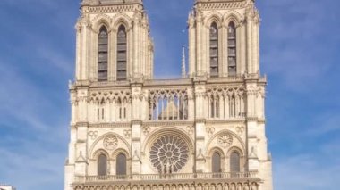 Notre Dame de Paris katedralinin ön cephesinde yürüyen insanlarla dolu bir meydan. Yazın mavi bulutlu gökyüzü
