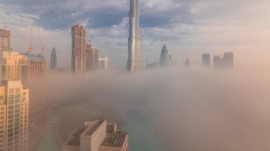 Dubai şehrinin hava panoramik görüntüsü sabahın erken saatlerinde sis zamanlarında. Gökdelenler ve gökdelenlerle dolu fütüristik şehir siluetinde gün doğumu. Güneş cam yüzeyden yansıyor