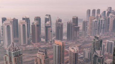 Şeyh Zayed Yolu yakınlarındaki JLT gökdelenleri ve marina kuleleri gece gündüz geçiş zamanı. Aydınlatılmış konut binaları ve villalarla ufuk çizgisi. Güneş doğmadan önce sisli bir sabah