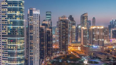 Dubai 'deki Business Bay Towers' dan gece gündüz geçiş zamanı. Gün batımından sonra inşaat halindeki bazı gökdelenlerin ve yeni binaların çatı manzarası. Işıklar yanıyor.