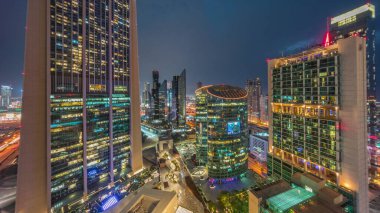 Dubai Uluslararası Finans Merkezi gökdelenleri hava gününden geceye geçiş zamanı. Gün batımından sonra yukarıdan gezinti güvertesi manzaralı aydınlık kuleler