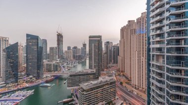 Kanal çevresindeki Dubai marina gökdelenlerinin hava görüntüsü. Günbegün yüzen tekneler ve gece geçiş zamanları. Günbatımından sonra beyaz tekneler yat kulübüne park edilir.