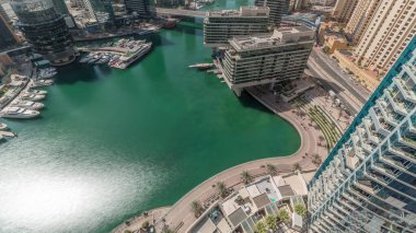 Kanal etrafındaki Dubai marina gökdelenlerine havadan bakıldığında gölgeler hızla ilerlerken yüzen teknelerin zamanlaması görülüyor. Beyaz tekneler yat kulübüne ve alışveriş merkezinin yakınına park edilmiş.