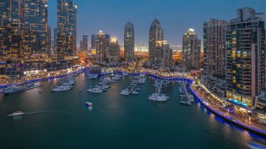 Dubai marinasındaki lüks yat hangarında, hava gününden geceye geçiş zamanı. Rıhtım boyunca modern gökdelenler ve limanda yüzen tekneler.
