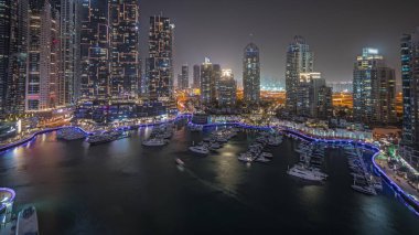 Panorama, Dubai marinasında gece hava sahasında lüks yat hangarını gösteriyor. Rıhtım boyunca modern gökdelenler ve limanda yüzen tekneler.