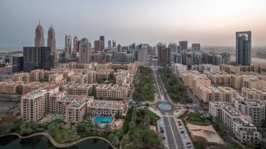 Barsha Heights bölgesindeki gökdelenler ve Greenens bölgesindeki alçak binalar gece gündüz panoramik zaman atlamaları. Palmiyeler ve ağaçlarla Dubai silueti