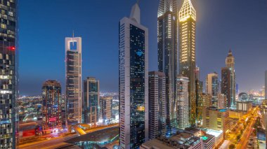 Günbatımından sonra Dubai Uluslararası Finans Bölgesi 'nin hava görüntüsü ve birçok gökdelen gece gündüz geçiş zamanı. Metro istasyonuyla çok katlı bir otoparkın yakınında trafik vardı. Dubai, BAE.