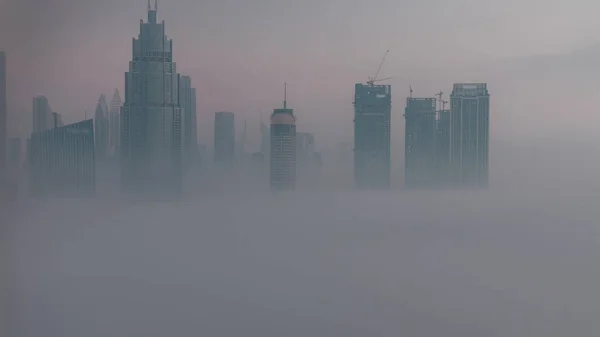 空中からの眺め朝の霧はドバイ国際金融センター地区の夜から昼への移行時間経過をカバーしました 日の出前に近代的な高層ビルがあるオフィスタワーとホテル — ストック写真