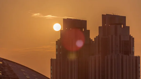 ドバイ国際金融センターの高層ビルの空中時間経過上の日没 背の高い塔と背景のオレンジ色の空の後ろに太陽が沈む — ストック写真