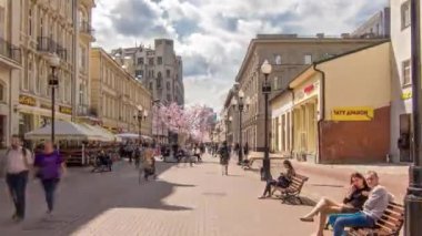Yerliler ve turistler Rusya 'nın başkenti Moskova' da ünlü yayalar Arbat Caddesi 'nde son sürat yürüyorlar. İnsanlar bankta oturuyor. Yaz gününde pembe ağaçlar ve mavi bulutlu gökyüzü