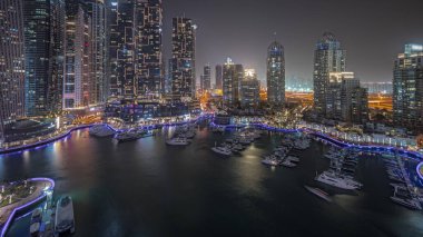 Panorama showing luxury yacht bay in the city aerial night  in Dubai marina. Modern skyscrapers along waterfront promenade and boats floating in harbor