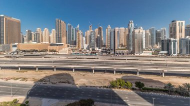 Panorama, Dubai Marina gökdelenlerini ve Şeyh Zayed yolunu metro antenli gösteriyor. Modern kulelerin yakınındaki bir otoyolda trafik var, Birleşik Arap Emirlikleri