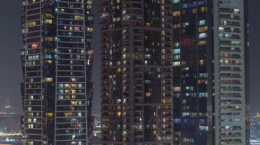 Şehrin hava zaman ayarlı yerleşim bölgesinde parlayan pencereleri olan uzun apartmanlar. Gökdelenlerdeki ve gökdelenlerdeki odalarda akşam ışığı