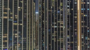 Şehrin hava zaman ayarlı yerleşim bölgesinde parlayan pencereleri olan uzun apartmanlar. Kulelerdeki dairelerin odalarında akşam ışığı ve aydınlatılmış gökdelenler