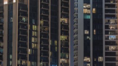 Şehrin hava zaman ayarlı yerleşim bölgesinde parlayan pencereleri olan uzun apartmanlar. Gökdelenlerdeki ve kulelerdeki dairelerde akşam ışığı