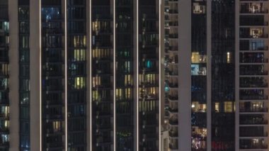 Şehrin hava zaman ayarlı yerleşim bölgesinde parlayan pencereleri olan uzun apartmanlar. Kulelerdeki ve gökdelenlerdeki odalarda akşam sarı ışığı