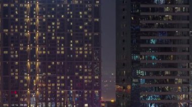 Şehrin hava akımının yerleşim bölgesinde parlayan pencereleri olan uzun apartman blokları. Büyük kulelerdeki ve gökdelenlerdeki odalarda akşam ışığı