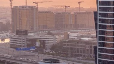 Dubai su kanalı çevresindeki inşaat alanında birçok vinç havadan zaman ayarlı. Evler ve villalar arkada. Otoyol köprüsünde trafik vardı. Gün batımında turuncu gökyüzü