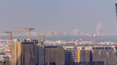 Dubai su kanalı çevresindeki inşaat sahasında sabahları çok sayıda vinç kullanılıyor. Palmiye adasının arkasında evler ve villalar var..