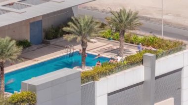 Havada geçen güneşli bir günde çatıda lüks bir yüzme havuzu. İnsanlar palmiyelerin altında mavi suyun etrafında dinleniyorlar. Manzarayı kapat. Yaz tatili ve tatil konsepti. Dubai, BAE