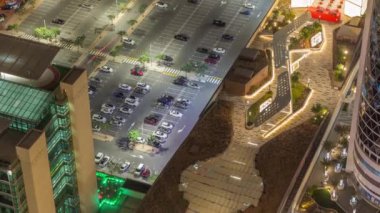 Otoparka park etmiş renkli arabaların hava manzarası. Park yerleri ve istikametler için çizgiler ve işaretler. Alışveriş caddesi yakınlarındaki Dubai finans bölgesi