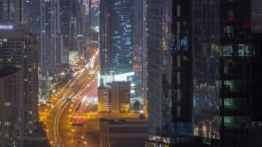 Tüm gece boyunca Dubai 'deki yoğun yol kavşağına yukarıdan hava görüntüsü. Arabalar iki yöne de doğru ilerliyor. Yüksek kuleleri olan iş sahası bölgesi