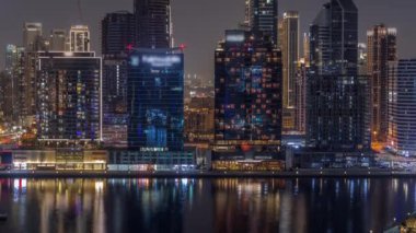 Dubai Business Bay ve şehir merkezinin havadan görüntüsü. Kanal gecesinde deniz kenarında parlayan pencereleri olan çeşitli gökdelenler ve kuleler. Vinçli inşaat alanı