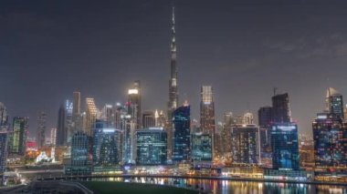 Dubai Business Bay ve şehir merkezinin havadan görüntüsü. Kanal boyunca çeşitli gökdelenler ve kuleler var. Vinçleri olan bir inşaat alanı. Karanlık gökyüzü