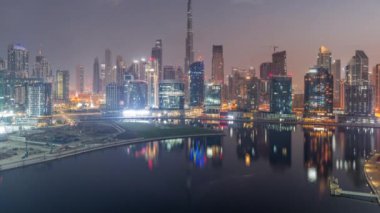 Dubai Business Bay ve Downtown 'ın havadan görüntüsü. Kanal boyunca çeşitli gökdelenler ve kuleler var. Gece gündüz geçiş zamanları. Güneş doğmadan önce vinçleri olan inşaat alanı