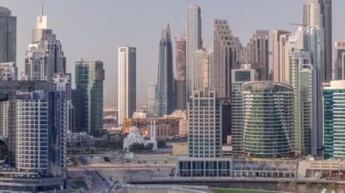 Dubai İşletme Koyu 'nun gökdelenleri ve su kanallarının zaman çizelgesi olan şehir manzarası. Rıhtımda konut ve ofis kuleleri olan modern gökyüzü. Yüksek binalarla çevrili bir cami.