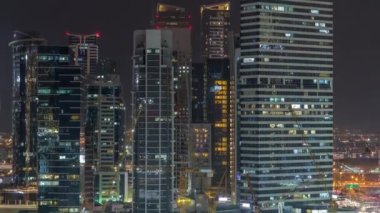 Dubai Business Bay 'in aydınlık gökdelenleri ve su kanalı hava gece zaman çizelgesine sahip şehir manzarası. Rıhtımda konut ve ofis kuleleri olan modern gökyüzü. Önde inşaat vinçleri