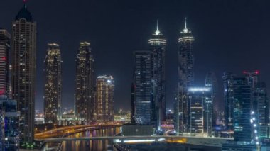 Dubai Business Bay 'in aydınlık gökdelenleri ve tüm gece boyunca su kanalı antenleri olan şehir manzarası. Rıhtımda konut ve ofis kuleleri olan modern gökyüzü. Ay batıyor