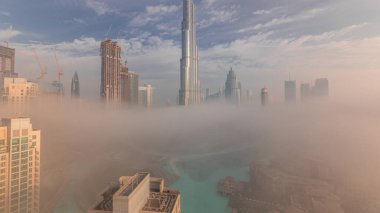 Sabahın erken saatlerinde sis sırasında Dubai şehrinin havadan panoramik görüntüsü. Gökdelenler ve gökdelenlerle dolu fütüristik şehir siluetinde gün doğumu. Güneş cam yüzeyden yansıyor