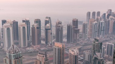 Şeyh Zayed Yolu yakınlarındaki JLT gökdelenleri ve marina kuleleri gece gündüz geçiş yapıyor. Aydınlatılmış konut binaları ve villalarla ufuk çizgisi. Güneş doğmadan önce sisli bir sabah