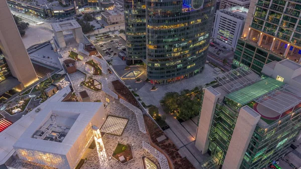 stock image Dubai international financial center skyscrapers and promenade on a gate avenue aerial day to night transition. Illuminated towers and mosque look down view from above