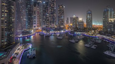 Panorama showing luxury yacht bay in the city aerial night in Dubai marina. Modern skyscrapers along waterfront promenade and boats floating in harbor