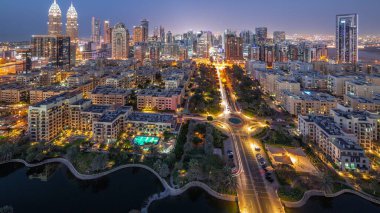 Barsha Heights bölgesindeki gökdelenler ve Greenens bölgesindeki alçak binalar günden geceye geçiş panoramik. Yol boyunca palmiyeler ve ağaçlarla Dubai silueti