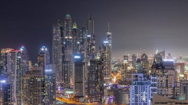Dubai Marina hava sahasının en yüksek bloğundaki çeşitli gökdelenlerin görüntüsü suni kanalla gündüz gece geçişi. Gün batımından sonra birçok kule ve yat