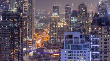 Dubai Marina ve Medya Şehri bölgelerinde modern gökdelenler ve ofis binaları günden geceye geçiş yapıyor. Yeşil park yakınlarındaki üst geçitte trafik ve kavşak.