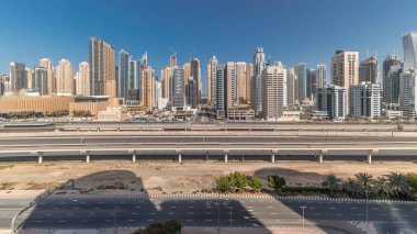 Panorama, Dubai Marina gökdelenlerini ve Şeyh Zayed yolunu metro antenli gösteriyor. Modern kulelerin yakınındaki bir otoyolda trafik var, Birleşik Arap Emirlikleri