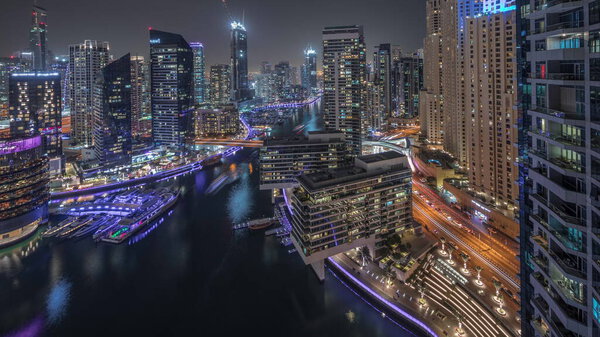 Panorama showing aerial view to Dubai marina illuminated skyscrapers around canal with floating yachts night. Towers in jlt and jbr districts. White boats are parked in yacht club