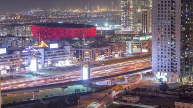 Aerial view to Dubai City Walk district night timelapse. New modern part with low rise buildings, arena and villas created as European-style streets. Construction site cranes and traffic on highway clipart