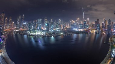 Dubai Business Bay ve Downtown 'ın gökdelenleri ve kuleleri kanal boyunca gece zaman çizelgesinde yer alan gökyüzü manzarası. Vinçli inşaat alanı