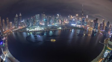 Dubai Business Bay ve şehir merkezinin havadan görüntüsü. Kanal boyunca çeşitli gökdelenler ve kuleler var. Tekneler ve yatlar suda yüzüyor. Vinçli inşaat alanı